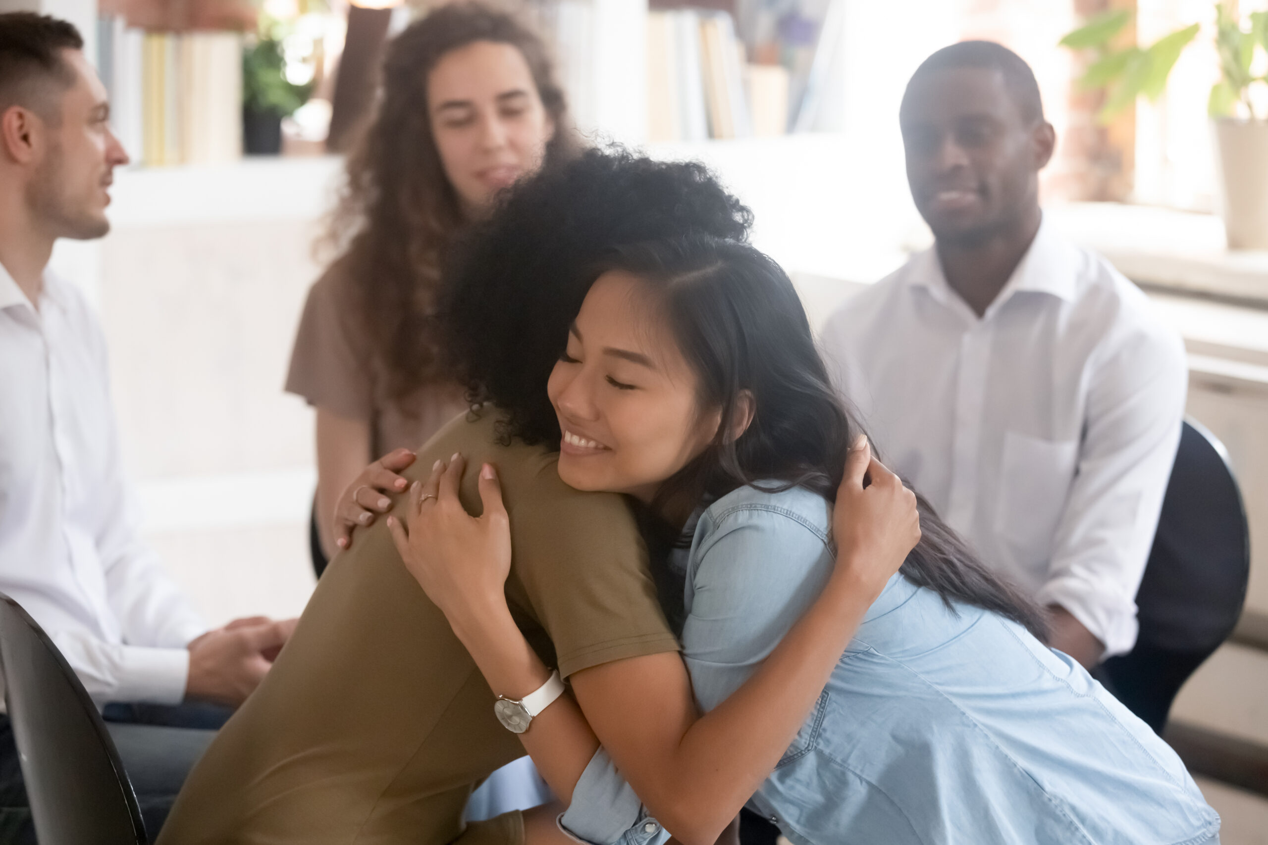 Asian and African women embracing giving psychological support during therapy