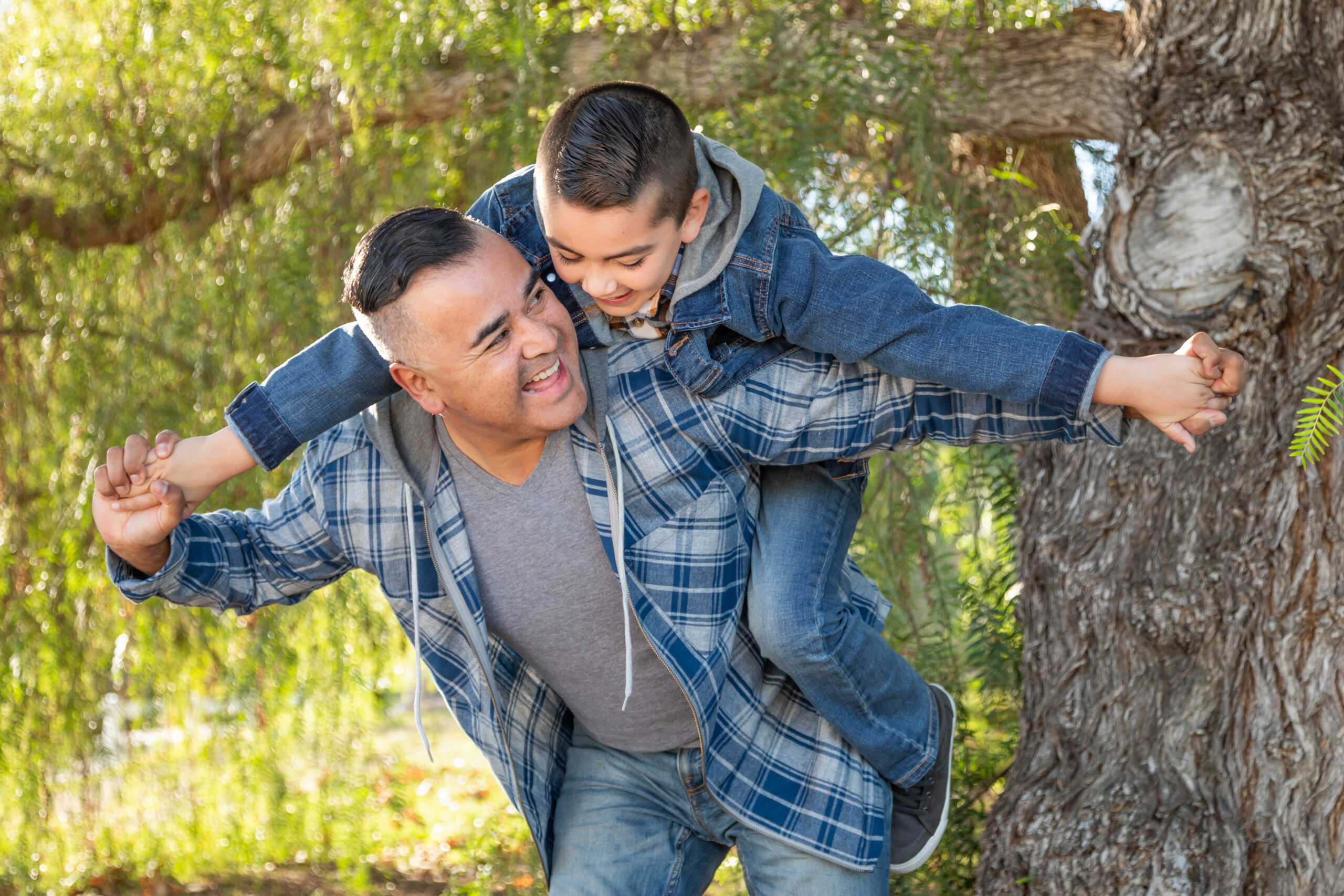 Mixed Race Father And Son Having Fun Piggy Back Outdoors.