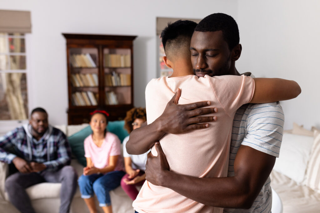 Supportive diverse male friends hugging each other at group therapy session