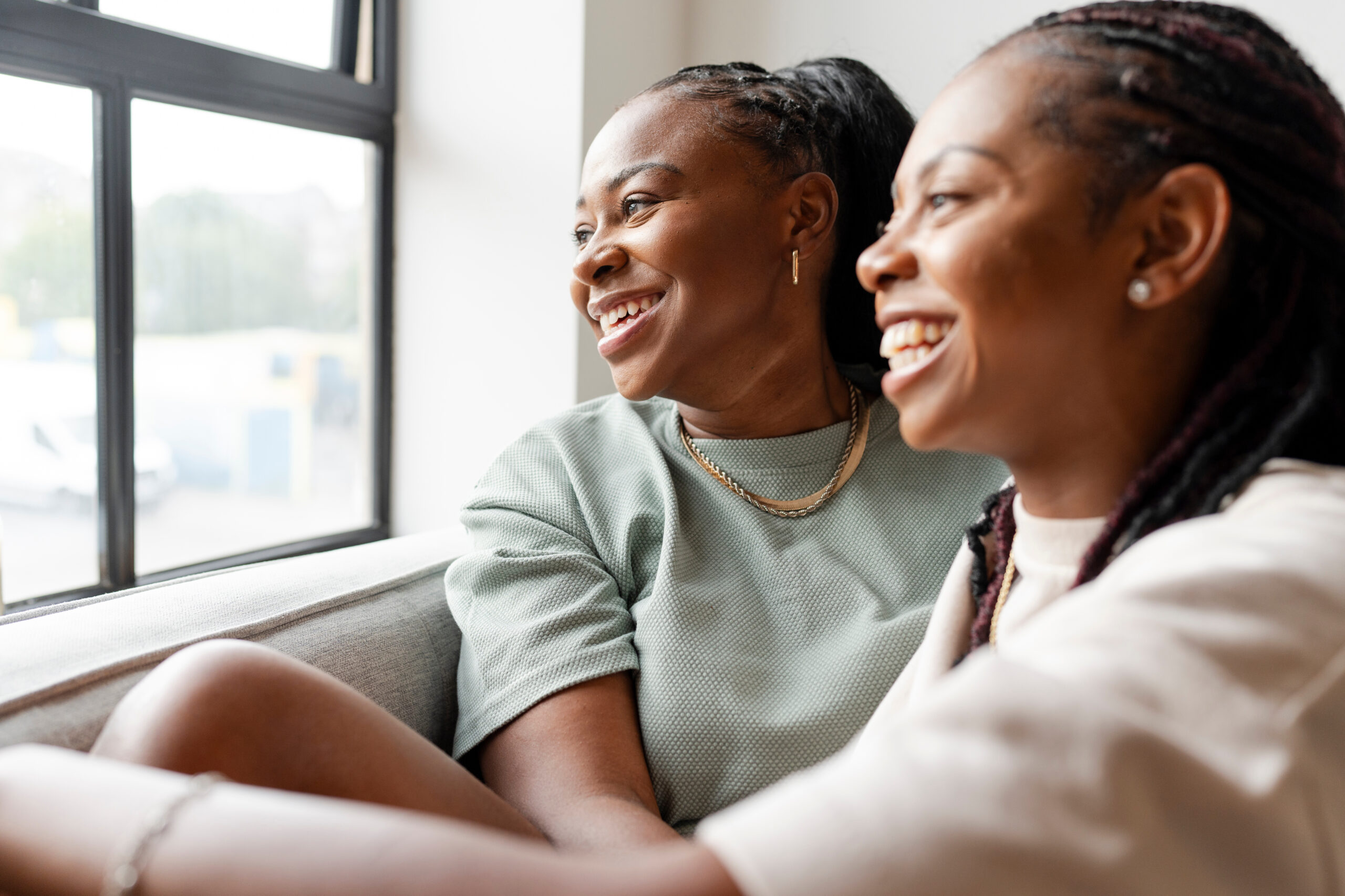 Portrait of happy lesbian couple looking through window at home