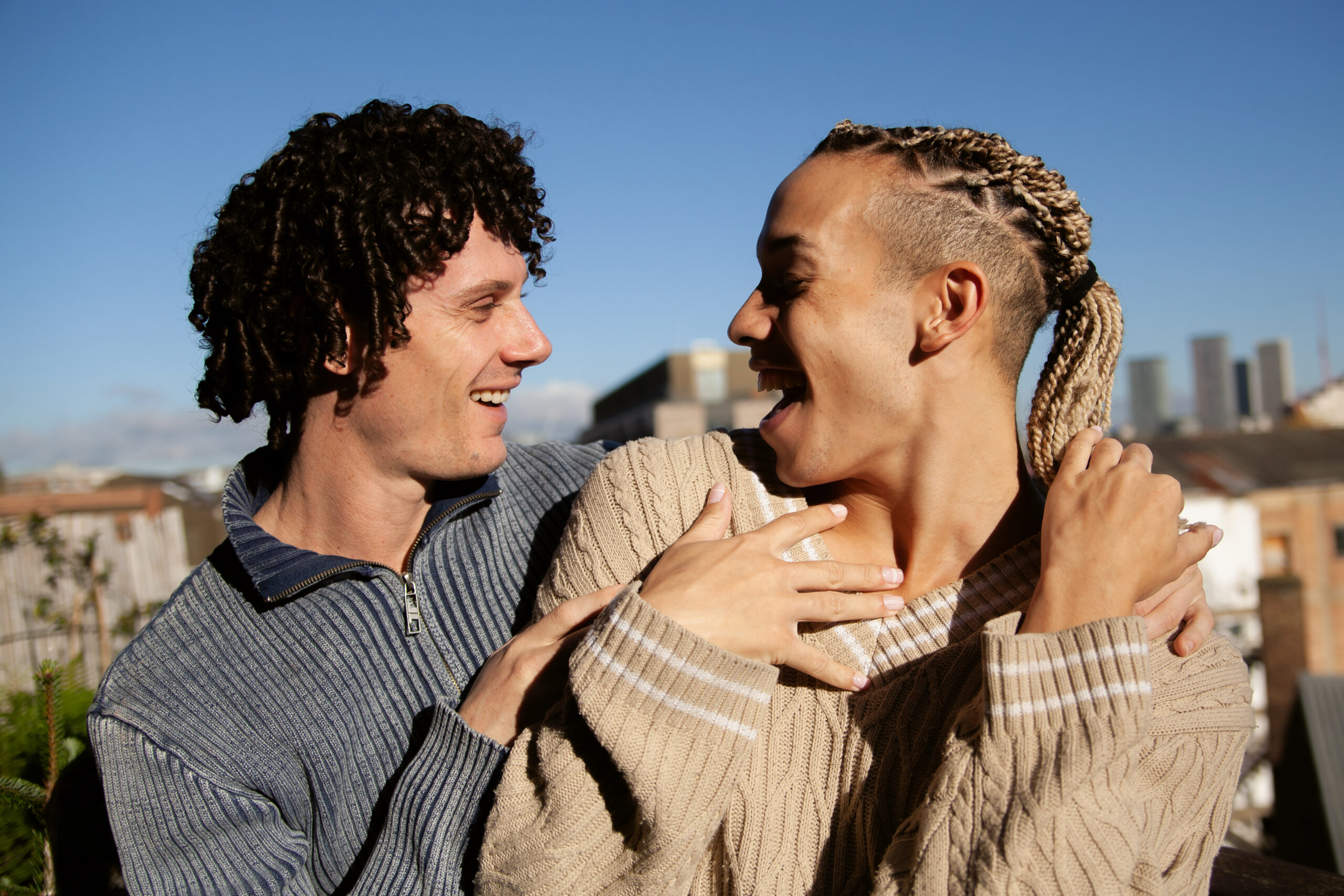 Portrait of two young multiracial men hugging on rooftop and smiling